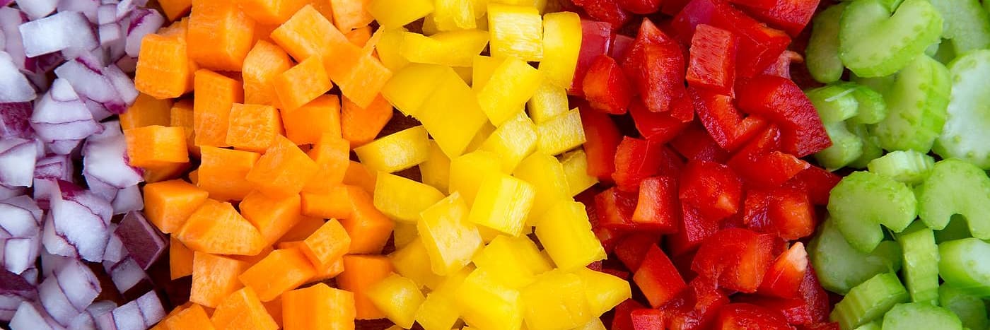 Five vegetables diced and pushed into separate bands across a board: red onion, carrot, yellow pepper, red pepper, celery
